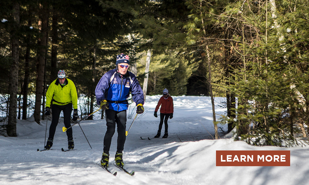 Three cross-country skiers skiing through the woods on groomed trails with a Learn More button.